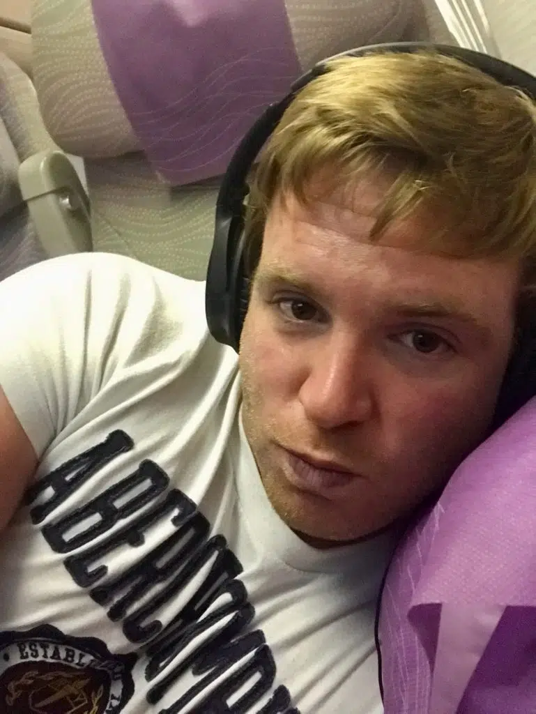 Trtl Pillow Test: Lohnt sich die Nackenstütze im Flugzeug? 5 Sascha lehnt im Flugzeug mit Kopfhörern an einem violetten Bordkissen