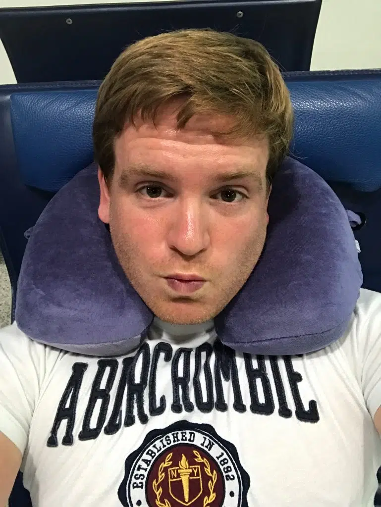 Trtl Pillow Test: Lohnt sich die Nackenstütze im Flugzeug? 3 Sascha mit klassischem U-förmigem Nackenkissen auf einem Flughafensitz