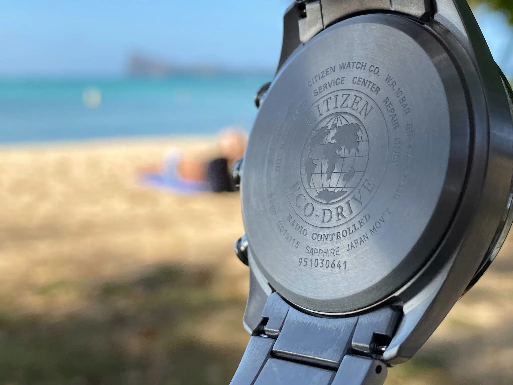 Citizen Eco-Drive Titanium CB5020-87L im Test: Erfahrungen nach Jahren 6 Gehäuseboden der Citizen Eco-Drive Titanium CB5020-87L vor unscharfem Strand und Meer