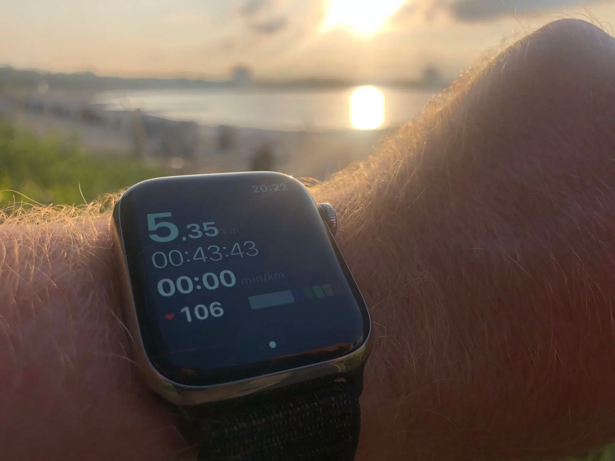 Apple Watch zeigt Laufdaten vor einer Bucht im Abendlicht
