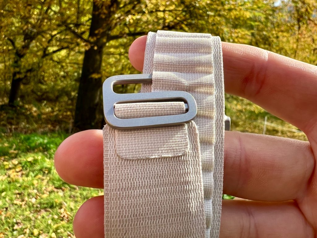 Auf dem Bild sieht man eine Großaufnahme des Titanium-Hakens des Apple Watch Ultra Alpine Loop, wie er halb in eine Schlaufe eingehängt ist. Das Armband ist über die Finger einer Hand gespannt, und im Hintergrund sieht man eine Grünfläche mit Bäumen. 

Das Armband hat sich in meinem Apple Watch Alpine Loop Test bewährt und hat gezeigt, was es kann. Foto: Sascha Tegtmeyer