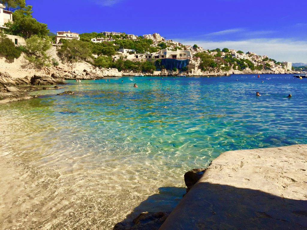 Auf dem Wasser sieht man aus der Perspektive vom Strand das herrlich klare und türkise Wasser der Bucht von Cala Fonels. 

Im Hintergrund sieht man die im Berg gebauten Villen.

Meine Großeltern waren begeistert, als sie in den 70er Jahren diese Bucht entdeckt haben – damals noch ganz auf eigene Faust, ohne googlen und Recherche im Internet. Foto: Sascha Tegtmeyer