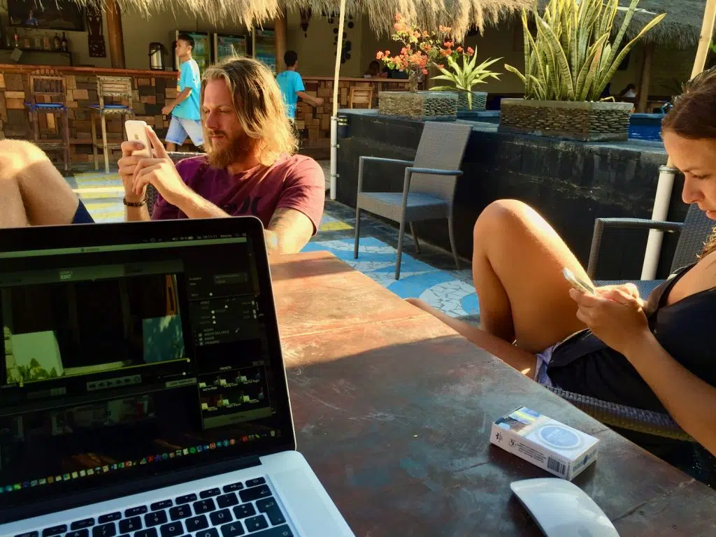 eSIM im Ausland mit dem iPhone: mein sicherer Ablauf 2 MacBook und zwei Reisende mit Smartphones in einer tropischen Hotelanlage