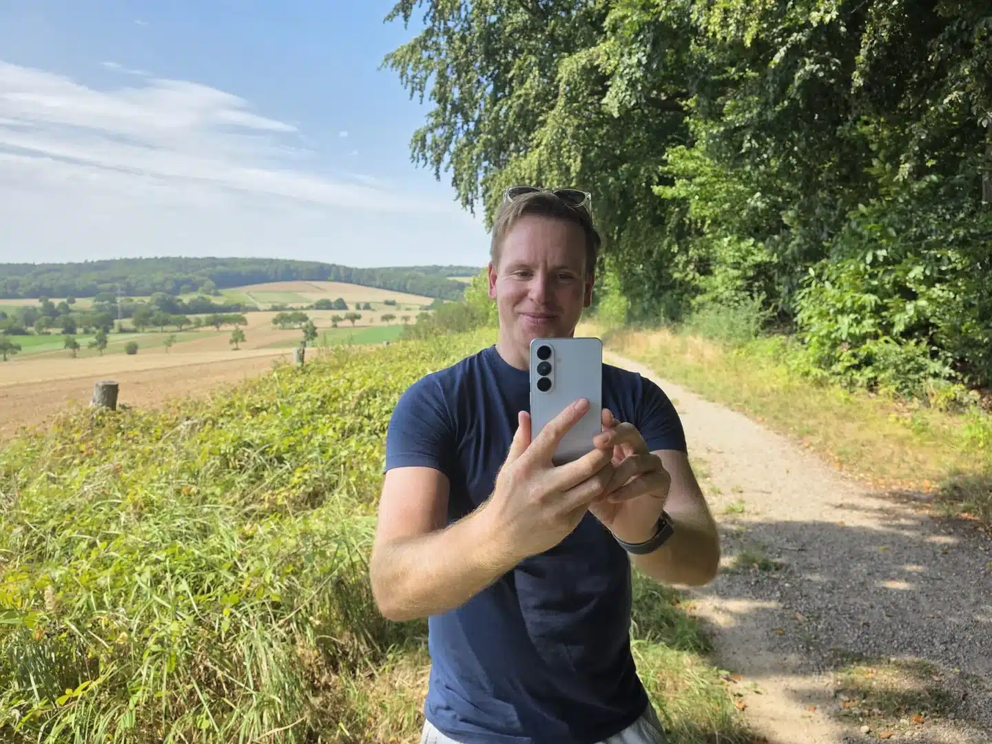 Samsung Hearapy im Test: Hilft der 100-Hz-Ton gegen Reiseübelkeit? 7 Sascha Tegtmeyer hält das hellblaue Samsung Galaxy S26 auf einem Feldweg