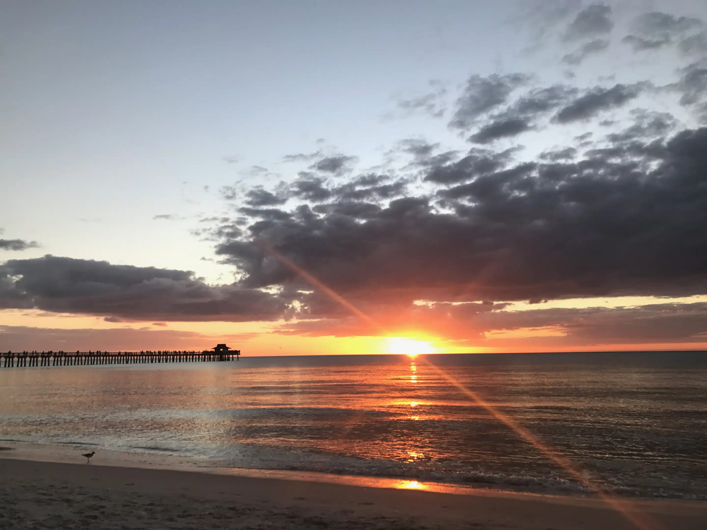 Naples in Florida: Strand und Abendlicht am alten Pier 9 Sonne am Horizont mit orangefarbener Spiegelung und Naples Pier links