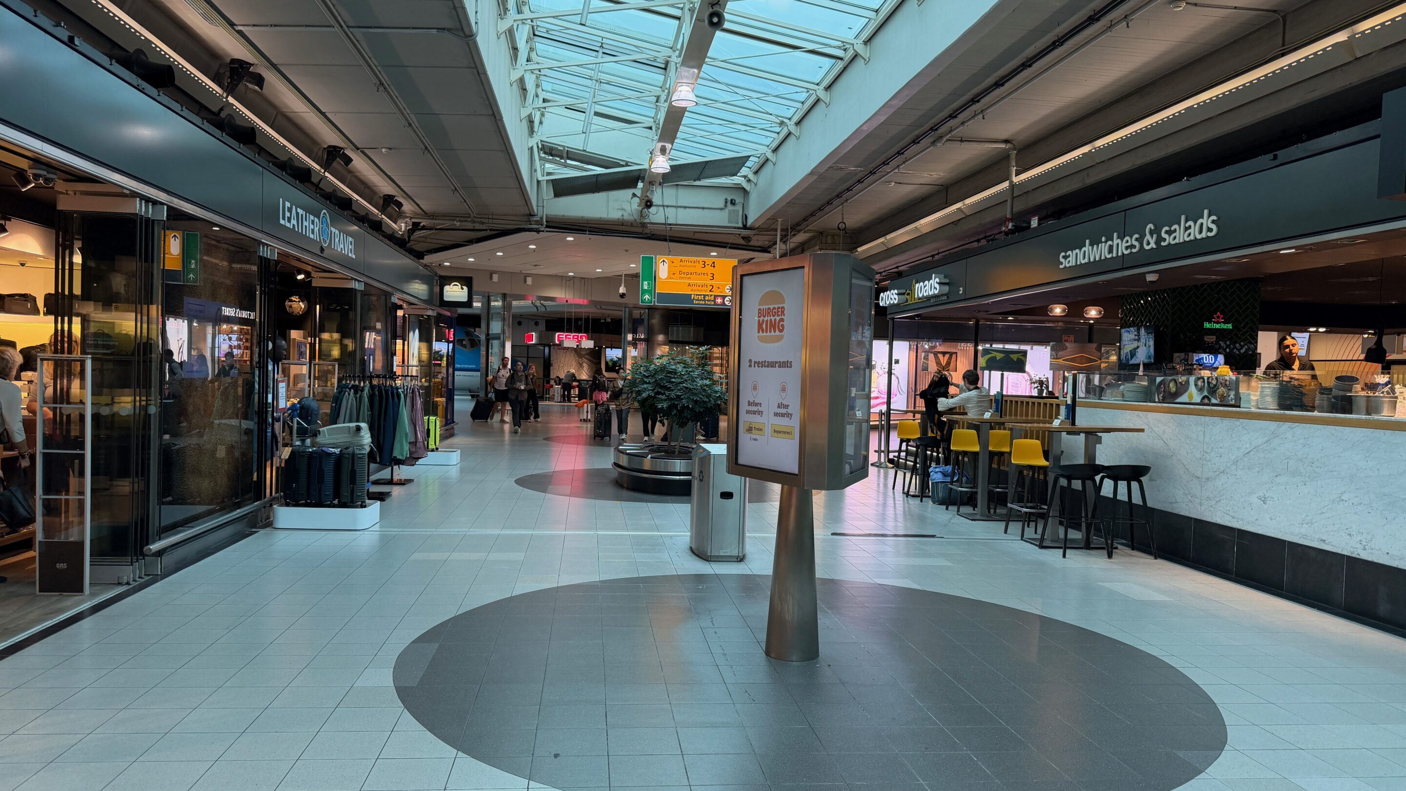 Flughafen Amsterdam Schiphol – meine Erfahrungen mit gut sechs Stunden Aufenthalt 4 Geschäfte und Gastronomie in einem überdachten Gang des Flughafens Schiphol